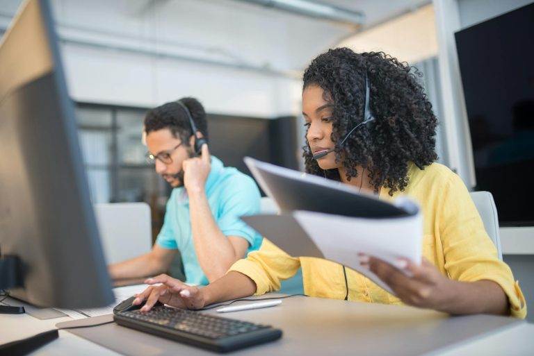 Two customer service representatives working with headsets in a modern office setting.